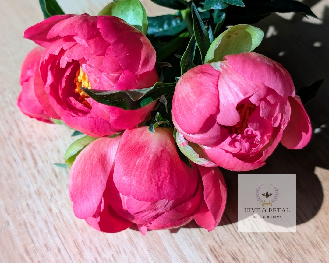 Bouquet of pink flowers on a wooden surface with 'Hive & Petal' branding.