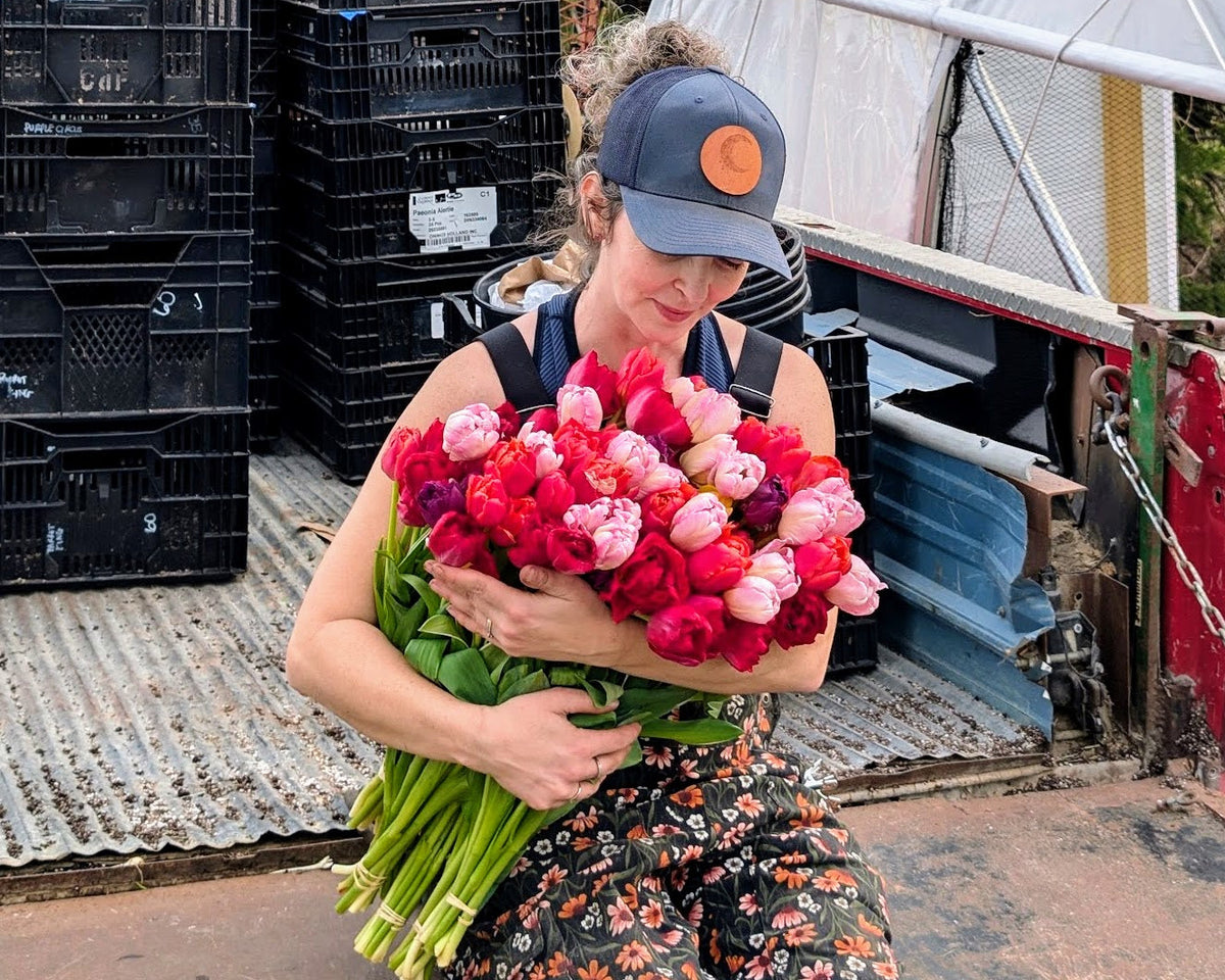 Person holding a bouquet of flowers in an outdoor setting with crates and equipment in the background