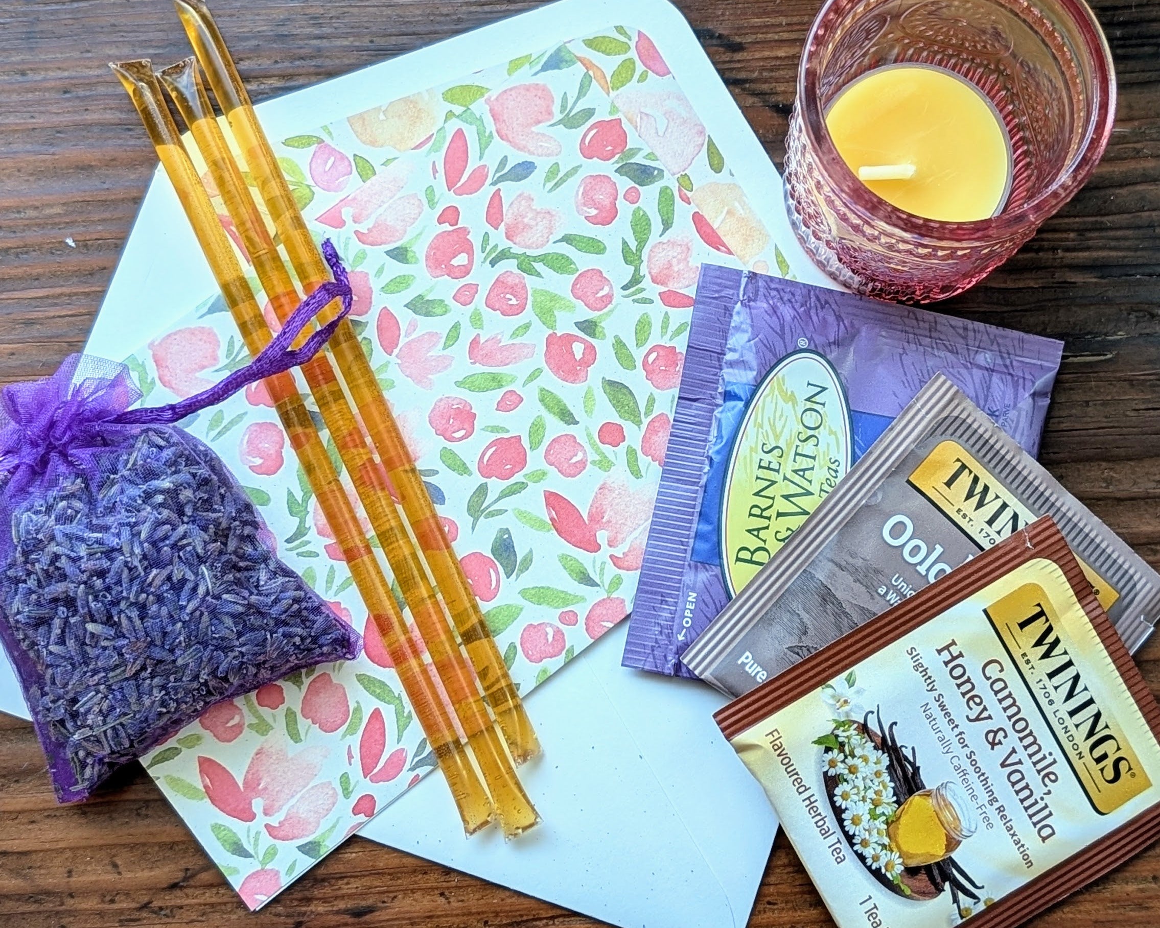 Assorted items including candles, a lavender bag, and tea packages on a wooden surface.