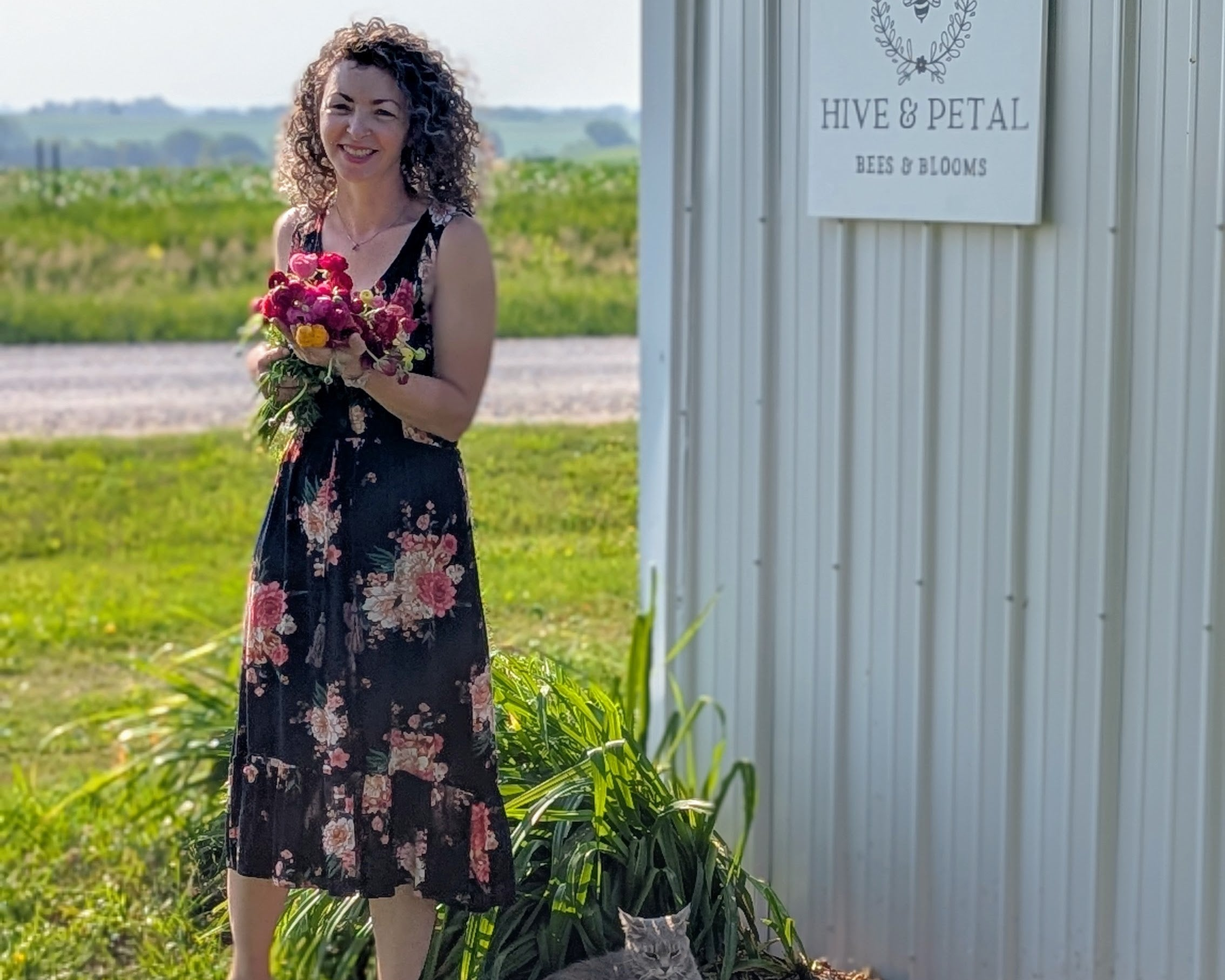Woman holding flowers standing next to a building with 'Hive & Petal' sign