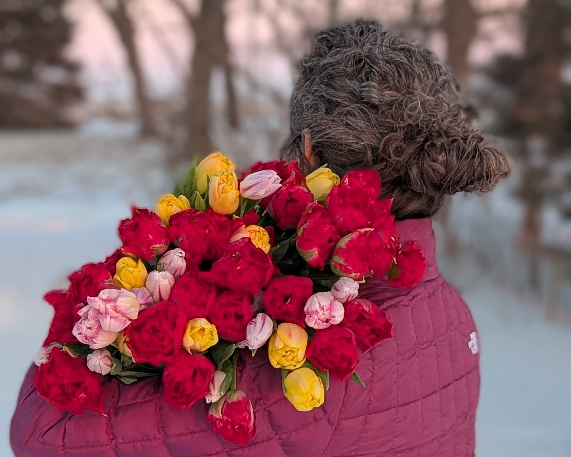 Person wearing a pink coat with a large bouquet of red, yellow, and pink flowers in a snowy landscape.
